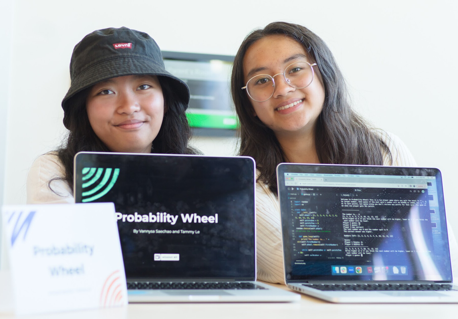 Two students sit at a desk. Their coding project is displayed on laptops in front of them