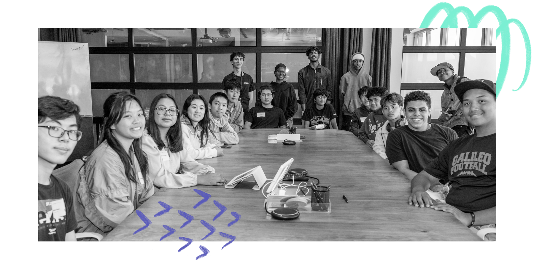 Black and white photo of a group of diverse computer science students sit around a wood board room table. 