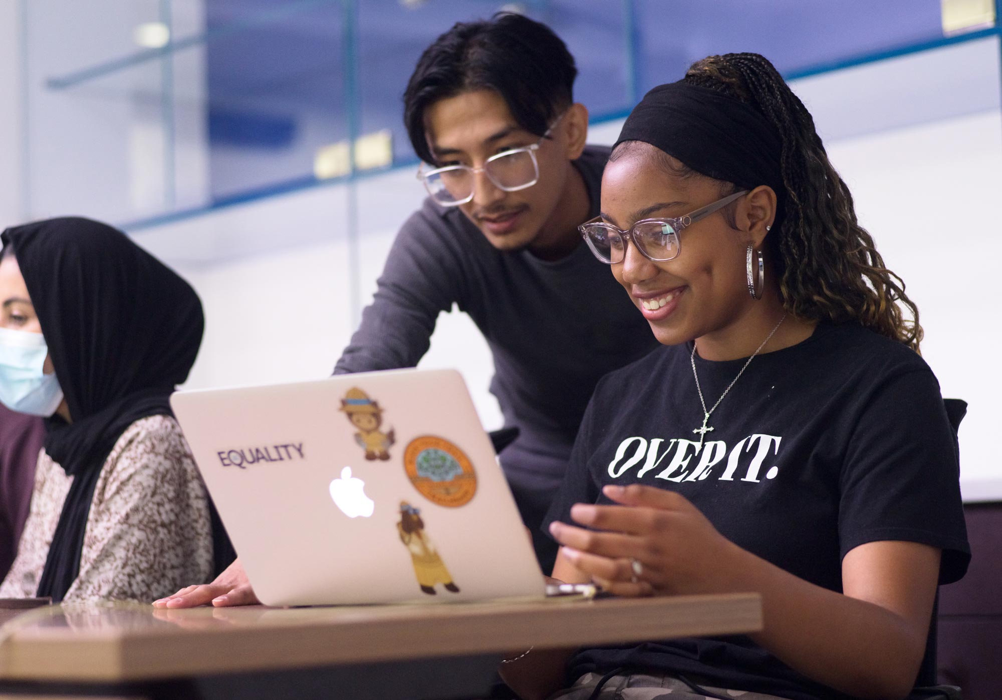 A young black female student is smiling while coding on her laptop. She is participating in a Mission Bit coding class.