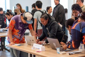 Students and community members collaborate on laptops during a Mission Bit technology showcase and coding event in San Francisco, exploring student-built projects and interactive computer science activities.